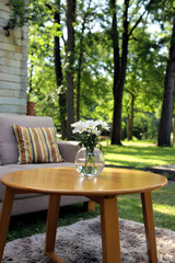 Fototapeta premium Outdoor daisies on table with sofa and trees in background, summer scene