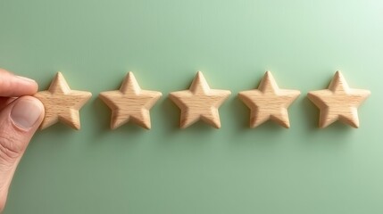 Hand places a wooden star, completing a row of five stars on a light green surface