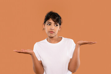 Woman expressing uncertainty while comparing options against an orange background during a casual...