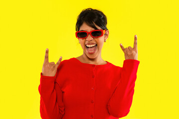 Young woman in red sweater and sunglasses expressing excitement against a vibrant yellow background...