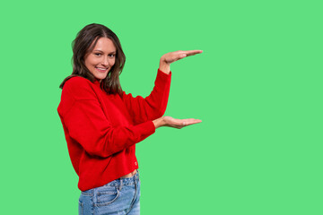 Smiling woman in red sweater showcases an empty space with hands in front of a bright green...
