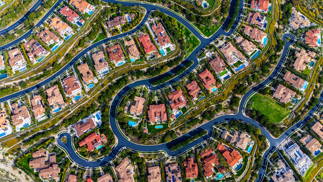 High-resolution aerial photograph showing a planned neighborhood with curved streets and luxury homes with red tile roofs and backyard swimming pools in Newport Beach, California. The community is sur