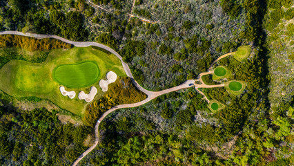 erial view of a golf course green with sand bunkers surrounded by natural shrubland in Newport Beach, California. The image captures a blend of manicured landscape and untamed wilderness, typical of S