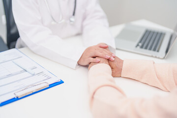 doctor holding hands with elderly female patient, showing empathy and support during a medical...