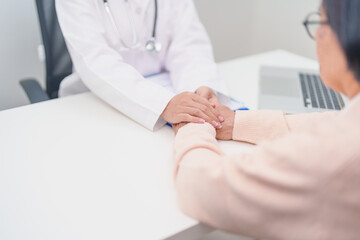 doctor holding hands with elderly female patient, showing empathy and support during a medical...