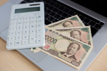 ノートパソコンの上に置かれた電卓と日本円紙幣のイメージ2