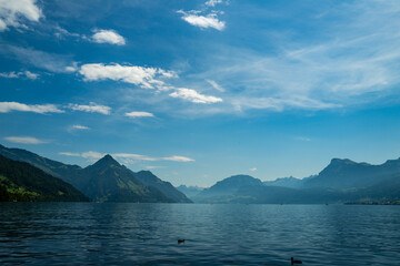 Alps mountain background. Swiss Alps mountain on sunny day. Mountain under clouds in blue sky. Blue nature background. Blue lake with sky near blue mountain.