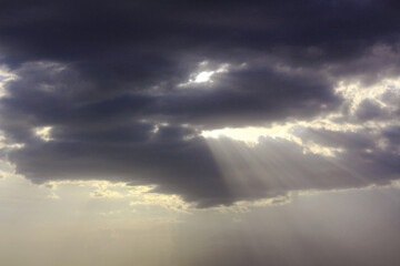 Obraz premium Sunbeams pierce through dark, dramatic clouds in a cloudy sky