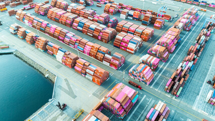 Aerial top view of organized stacks of colorful shipping containers at a busy cargo yard. The image reflects the logistics efficiency and volume of global trade through maritime transport.