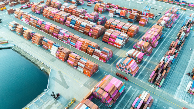 Aerial top view of organized stacks of colorful shipping containers at a busy cargo yard. The image reflects the logistics efficiency and volume of global trade through maritime transport.