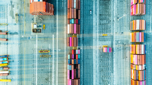 Top-down aerial photo of a container yard showing neatly arranged cargo containers, internal roads, and loading equipment. The image emphasizes the structured nature of global logistics systems.