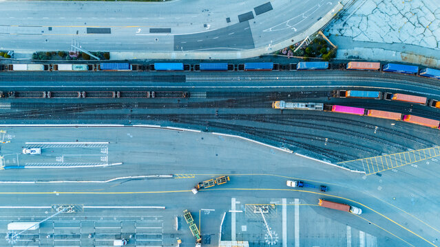 Aerial image showing railway lines, freight trains, and trucks operating at a cargo port. The infrastructure highlights intermodal logistics, connecting sea freight with land transportation.
