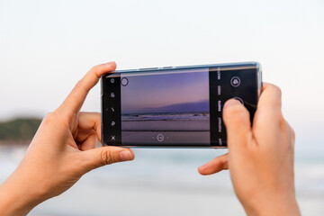 A girl is taking pictures with her phone while traveling at the seaside