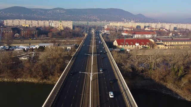 Straight road and tracks lead into Budapest skyline during golden sunset, drone flyover