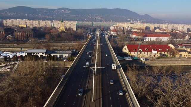 Aerial angle shows Budapest tracks and roads converging into bridge over Danube at sunset