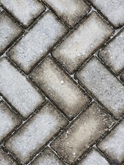 Background of a walkway or pavement with a herringbone-patterned gray tiled surface