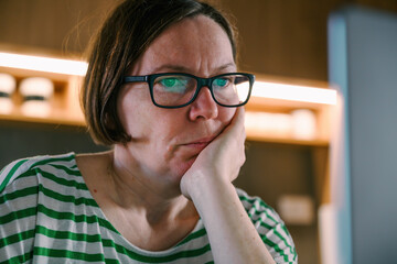 Portrait of adult female freelancer with eyeglasses working online at her home office on a laptop computer