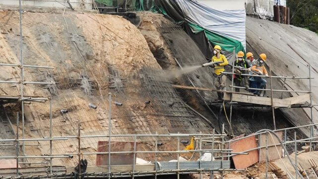 Workers in safety gear applying shotcrete on on hillside for slope stabilization.