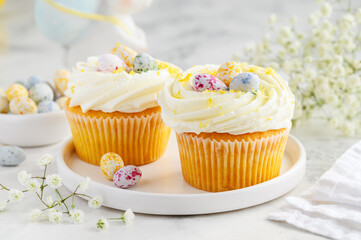 Two Easter lemon cupcakes with cream, lemon curd inside and candy eggs. Festive happy easter concept. Selective focus
