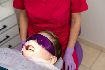 Child enjoying a dental checkup with a smiling expression, wearing protective eyewear while seated...