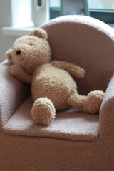 Adorable soft brown teddy bear sitting alone on a chair in a cozy indoor setting. The plush toy creates a sense of warmth, nostalgia, and childhood memories. Ideal for themes related to childhood.