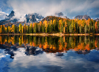 Fototapeta premium Huge peaks and colorful larch trees reflected in the calm waters of Antorno lake. Dramatic autumn scene of Dolomite Alps, National Park Tre Cime di Lavaredo, Italy. 
