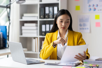 Serious female accountant working with financial documents in office and auditing accounts. Auditor checking financial report documents on desk.