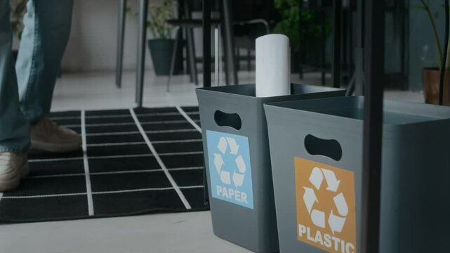 Low section shot of unrecognizable man walking through modern sustainable office with organized waste management, then throwing paper into designated recycling bin during workday