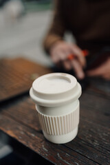 White reusable coffee cup standing on wooden table in a cafe