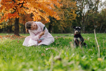 Fototapeta premium Girl taking pictures of dog on leash in autumn park