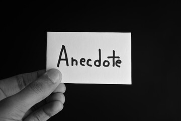Hand holding a paper card with the word ANECDOTE