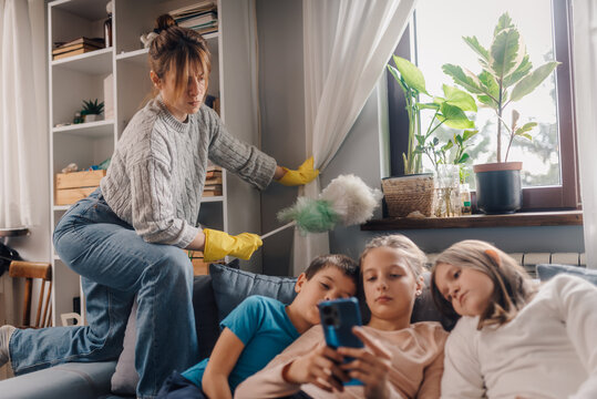 Mother dusting while children using smartphone on sofa