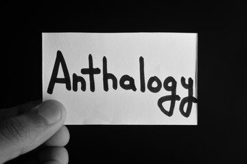 Hand holding a paper card with the word ANTHALOGY