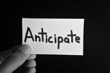 Hand holding a paper card with the word ANTICIPATE