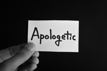 Hand holding a paper card with the word APOLOGETIC