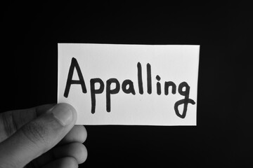 Naklejka premium Hand holding a paper card with the word APPALLING