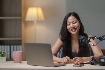 Young asian woman recording podcast from her cozy home office, using professional microphone and...