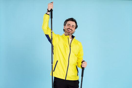 Smiling hiker holding trekking poles on blue background