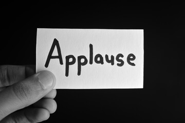 Hand holding a paper card with the word APPLAUSE