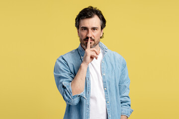 Bearded man making silence gesture on yellow background
