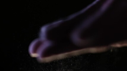 Close-up of hand sprinkling flour against dark background