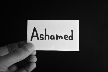 Hand holding a paper card with the word ASHAMED