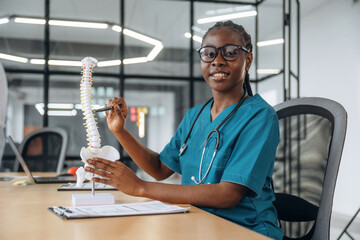 Detailed explanation of human spine model. Female doctor in coat is in the office clinic