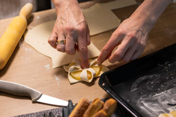 A woman wraps a pineapple wedge in puff pastry. Baking