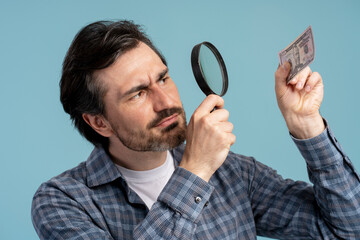 Man inspecting twenty dollar bill with magnifying glass on blue background