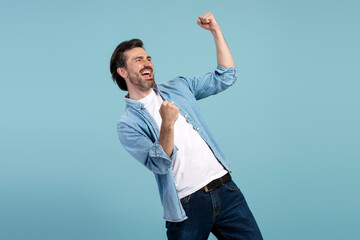 Excited man celebrating success with raised fists on blue background