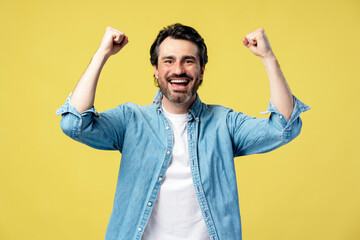 Excited man celebrating with raised fists on yellow background