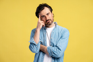 Pensive man touching head and reflecting on yellow background