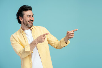 Cheerful man pointing aside with both index fingers on blue background