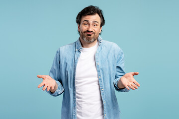 Confused man shrugging shoulders gesturing i don't know on blue background